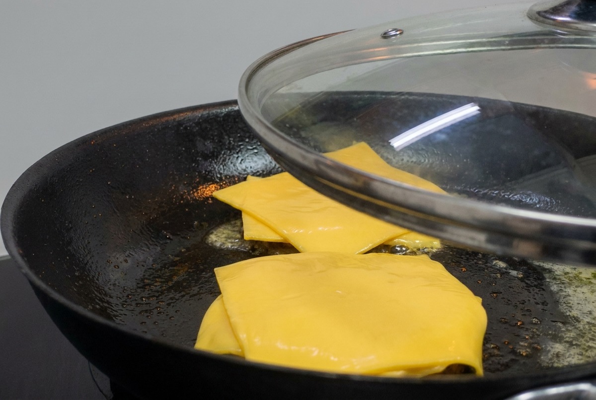 Un couvercle en verre posé sur une poêle contenant des steaks garnis de fromage fondant.