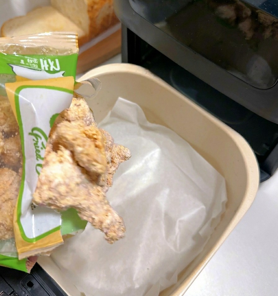 Morceaux de poulet pané surgelés versés dans le panier dune friteuse à air tapissé de papier cuisson.