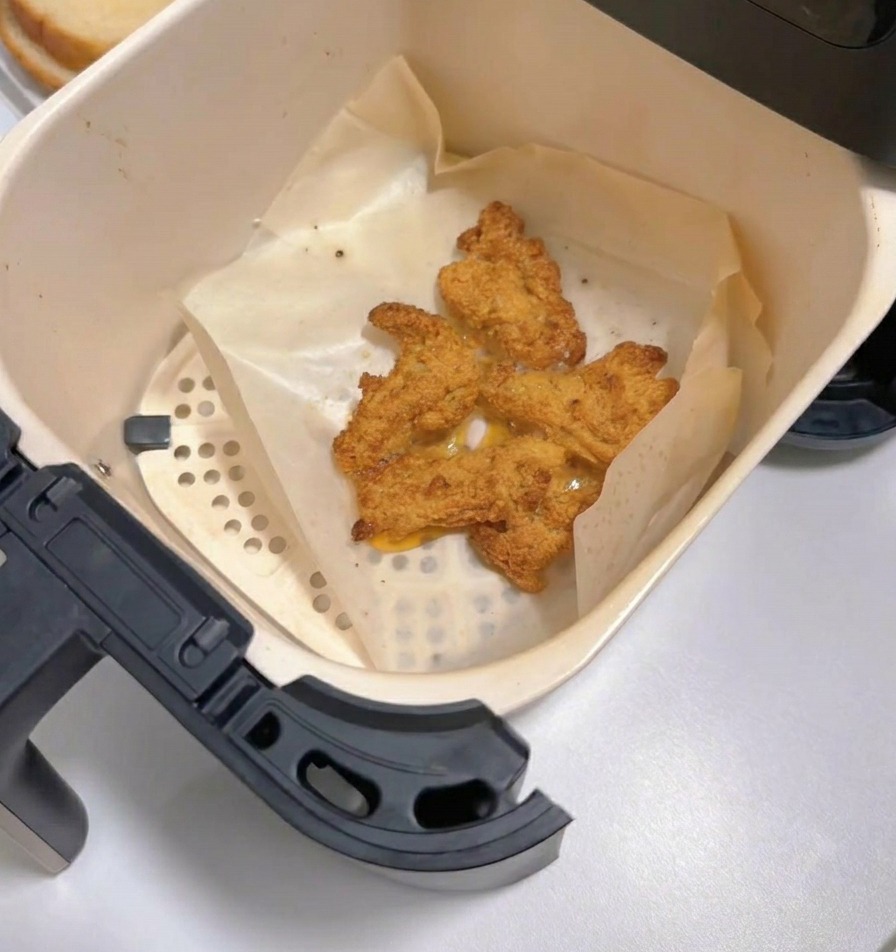 Tiroir de friteuse à air ouvert montrant plusieurs morceaux de poulet frit doré et croustillant sur du papier cuisson.
