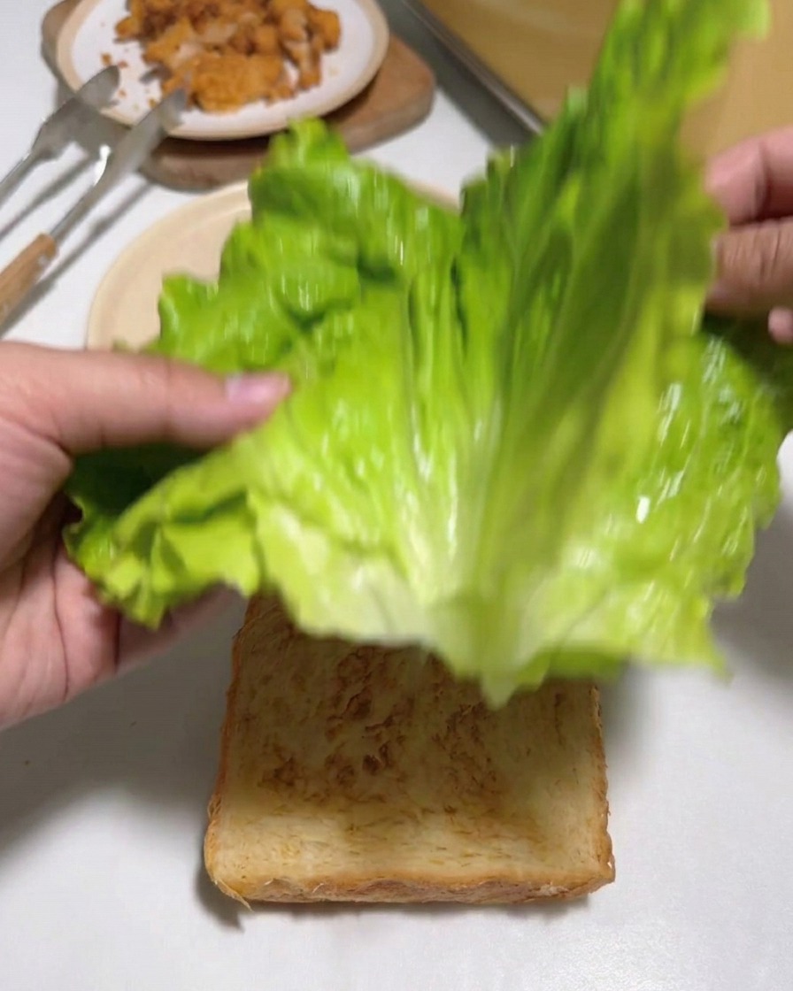 Mains déposant de grandes feuilles de laitue verte fraîche sur une tranche de pain grillé.