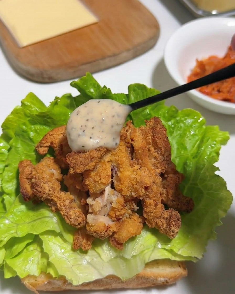 Une cuillère versant de la mayonnaise crémeuse au poivre et yuzu sur du poulet frit haché et de la laitue.