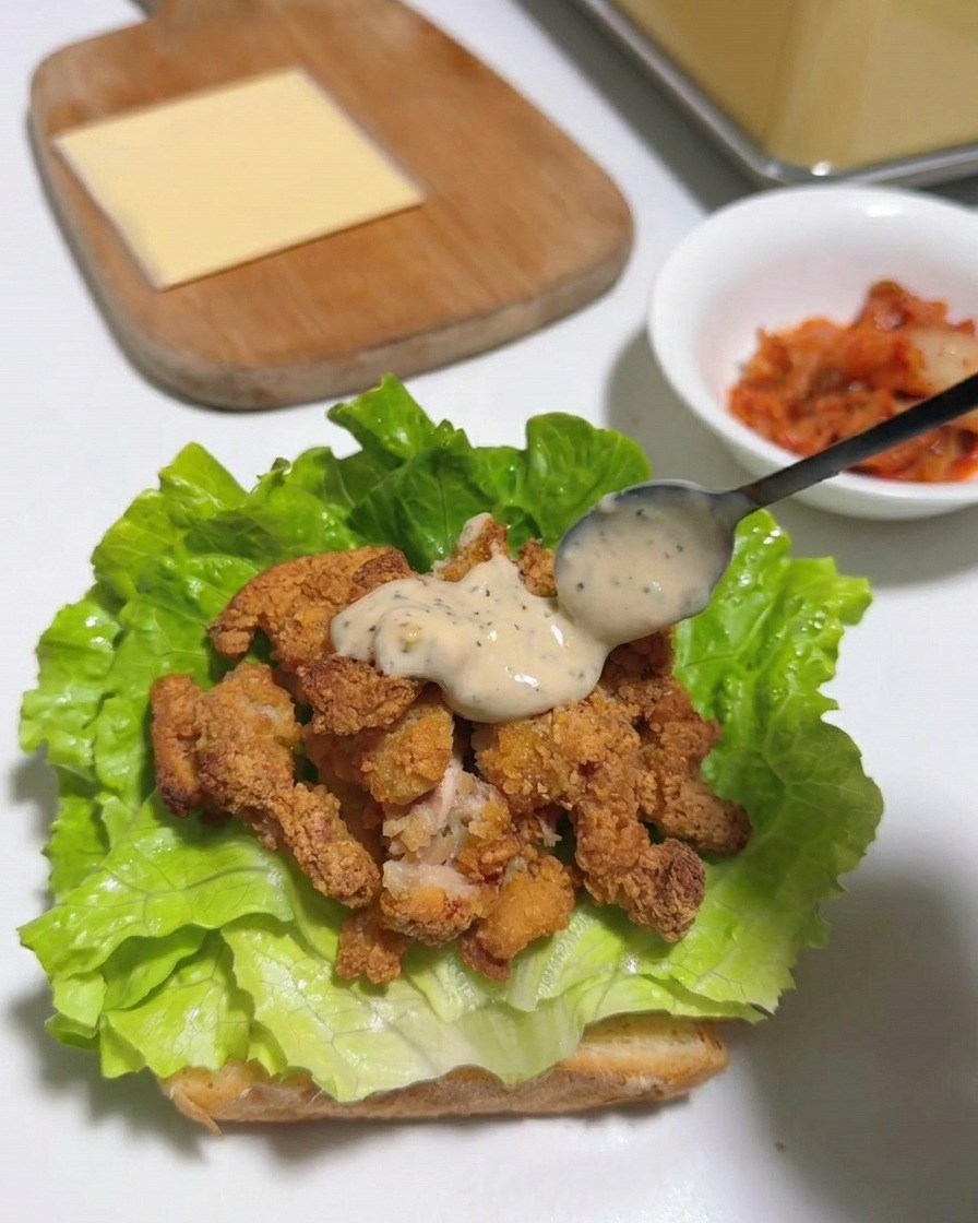 Une tranche carrée de fromage jaune posée sur le poulet frit nappé de sauce et la laitue.