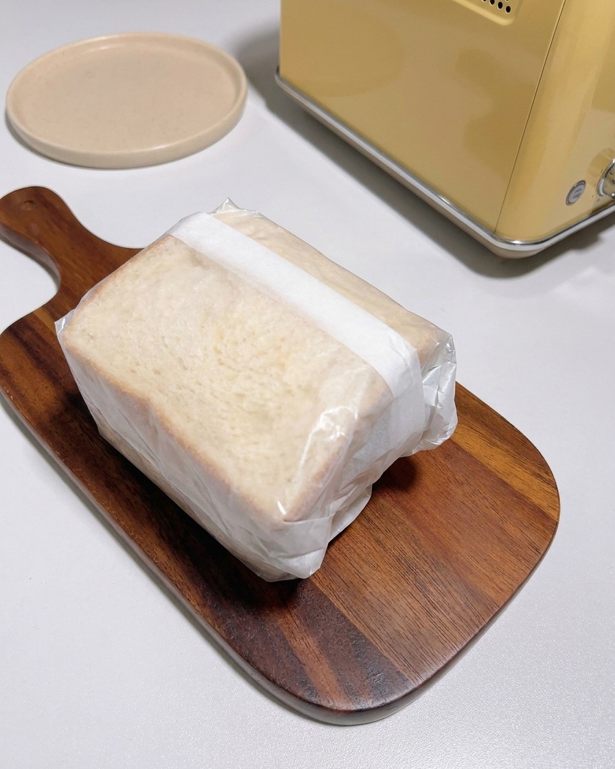 Un sandwich épais étroitement enveloppé dans du papier cuisson translucide posé sur une planche en bois.