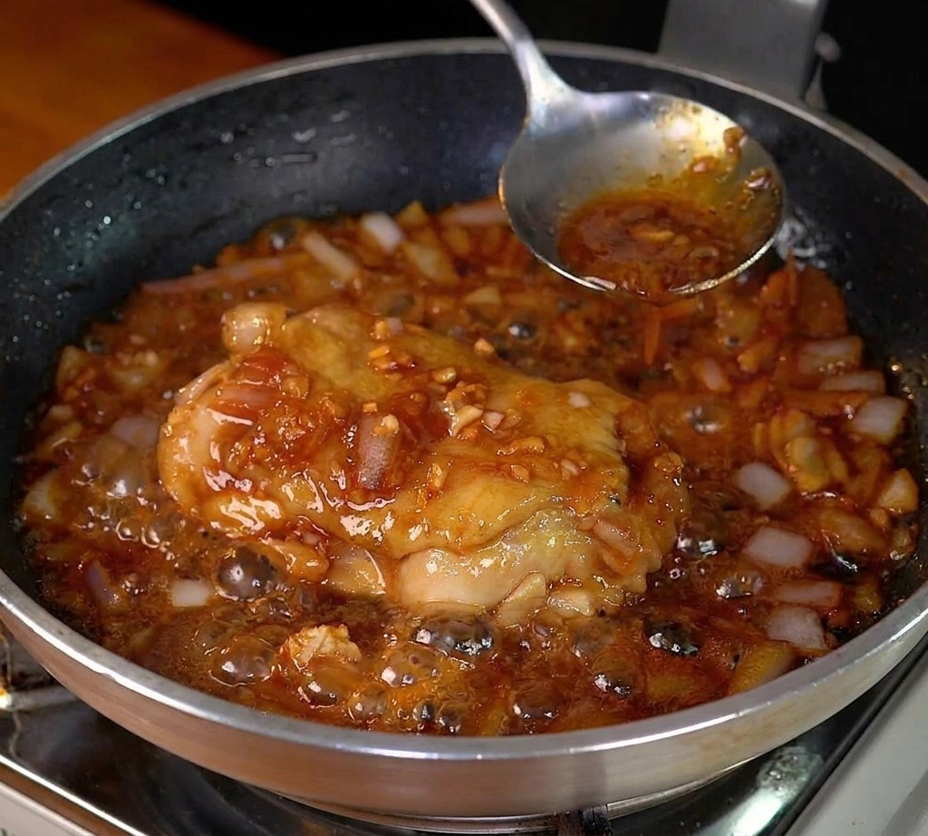 Haut de cuisse de poulet mijotant dans une sauce sombre et bouillonnante avec des oignons.