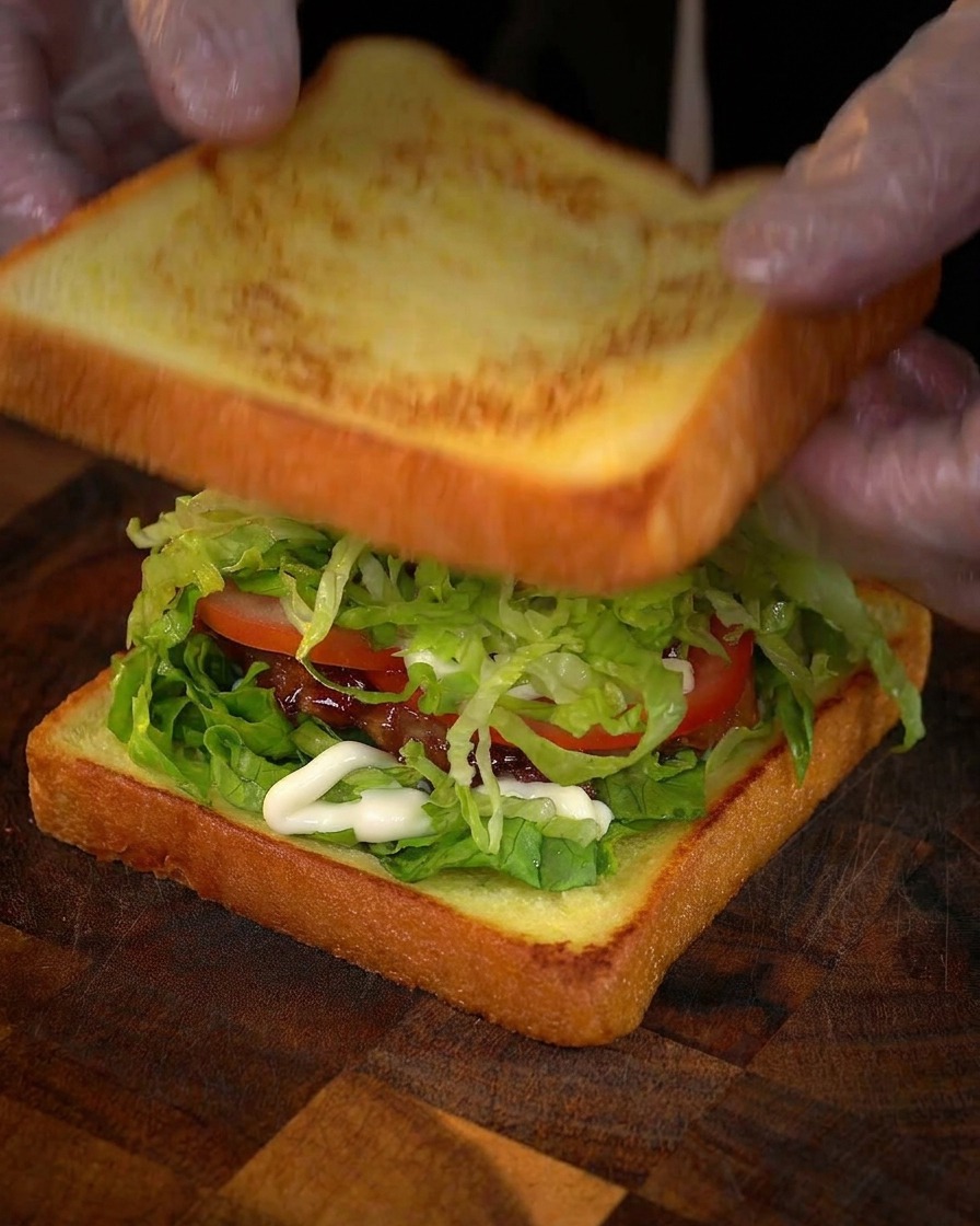 Des mains posant la dernière tranche de pain doré sur le sandwich garni.