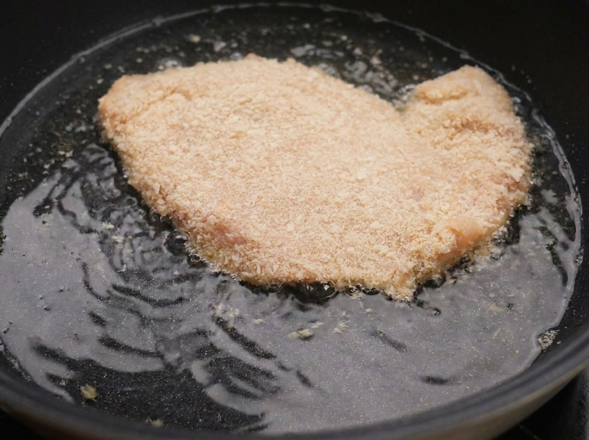Un blanc de poulet pané frémissant dans lhuile chaude dune poêle noire.