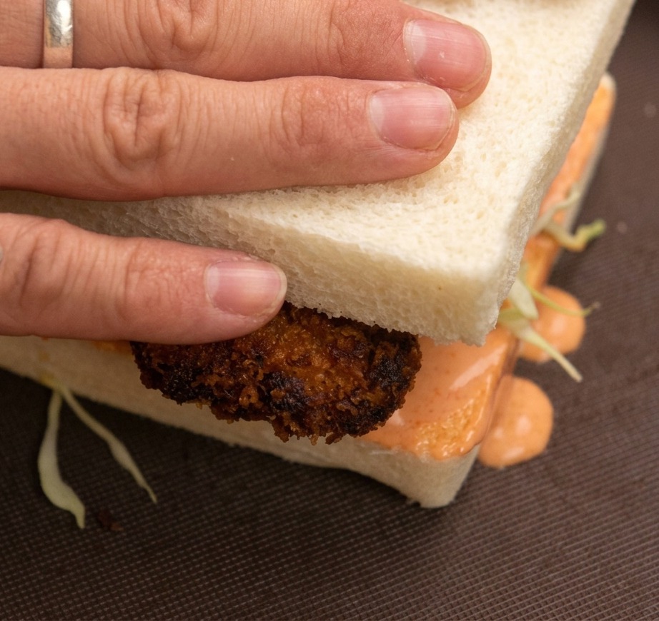 Des mains pressant le haut dun sandwich au poulet frit.