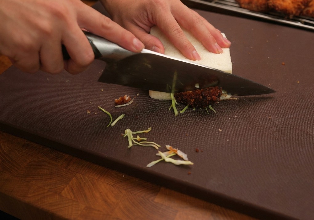 Un couteau de cuisine tranchant un sandwich au poulet épais sur une planche.