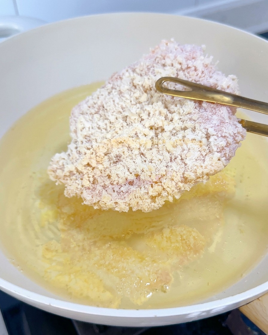 Une escalope de poulet panée surgelée plongée dans de lhuile bouillante avec des pinces dorées.