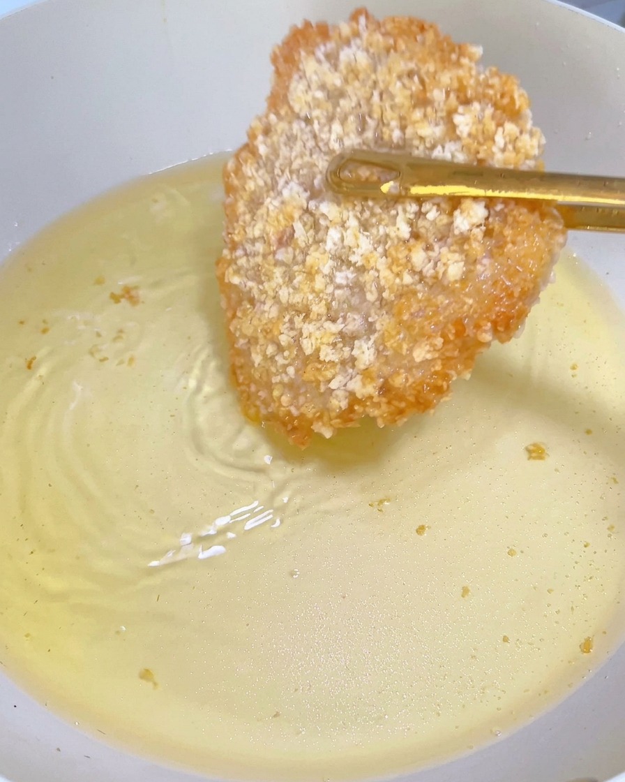 Escalope de poulet à la croûte dorée retournée avec des pinces dans une poêle.