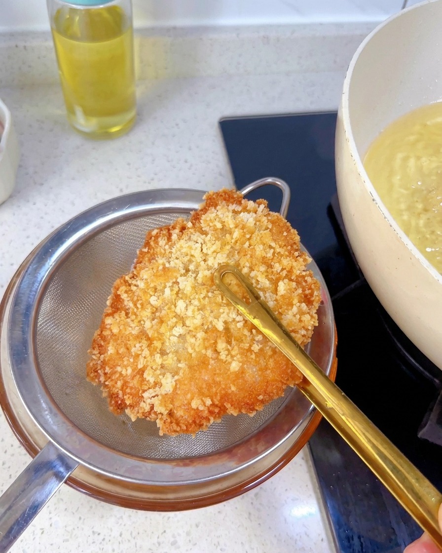 Une escalope de poulet bien dorée tenue au-dessus dune passoire métallique pour éliminer lexcès dhuile.