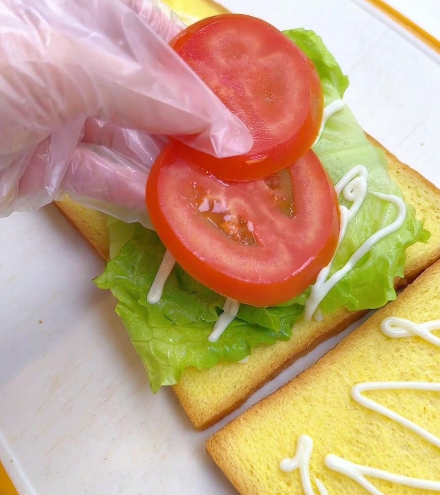 Doigts déposant deux rondelles de tomate rouge sur la laitue.