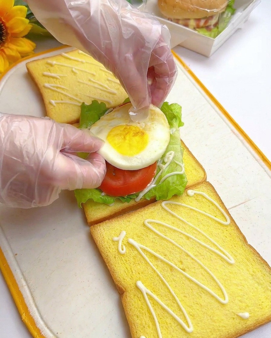 Mains déposant un œuf au plat sur les tomates et la laitue.
