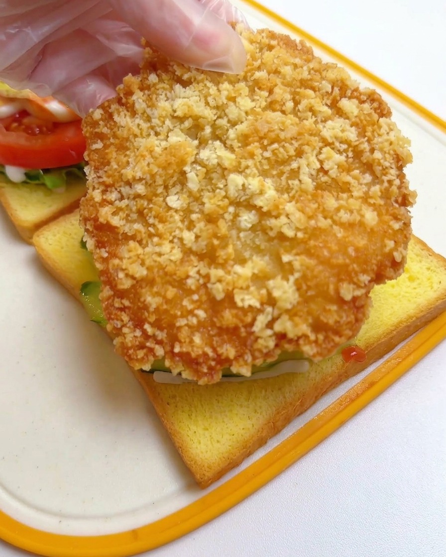 Main déposant une large escalope de poulet frit sur les concombres.