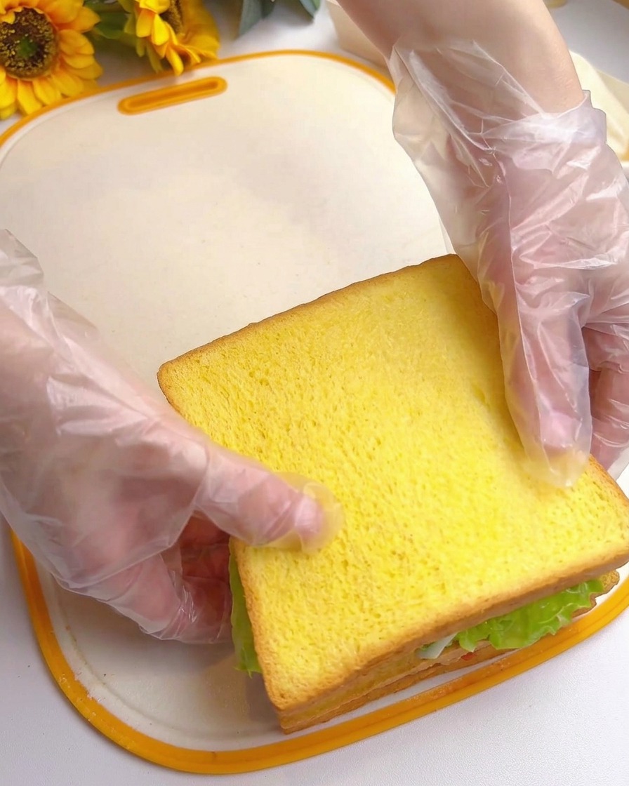 Deux mains pressant le dessus du sandwich multi-étages terminé.