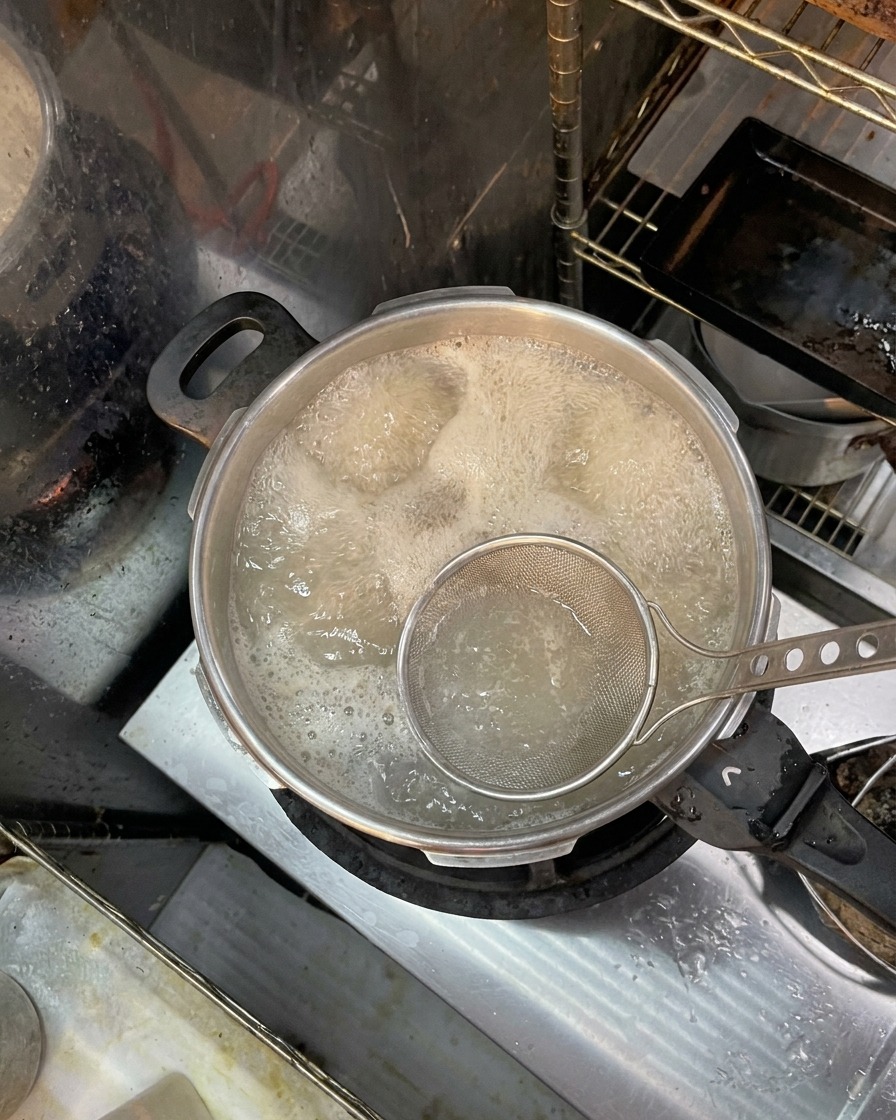 Une écumoire retirant la mousse brune à la surface de leau bouillante contenant les os.