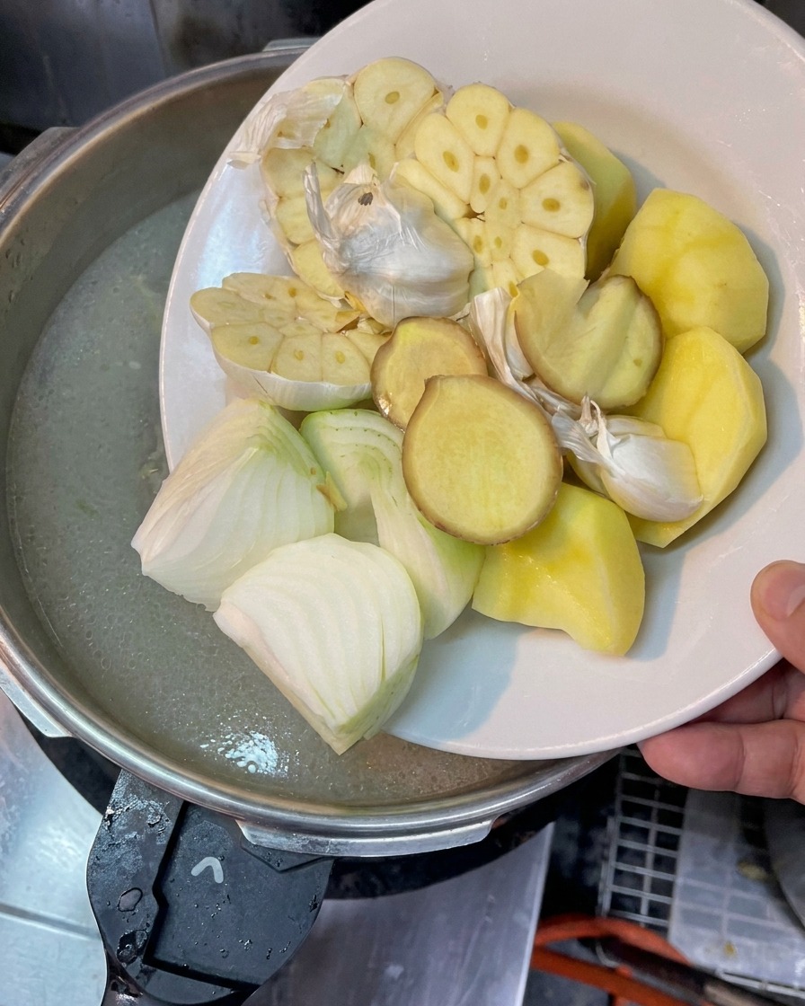 Une assiette avec de lail coupé, des oignons, du gingembre et de la pomme de terre au-dessus du bouillon.