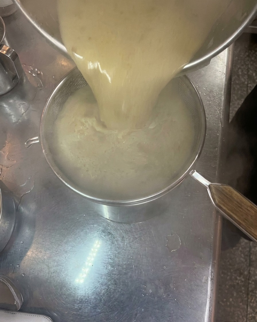 Bouillon tonkotsu crémeux versé à travers une passoire fine dans une autre marmite.