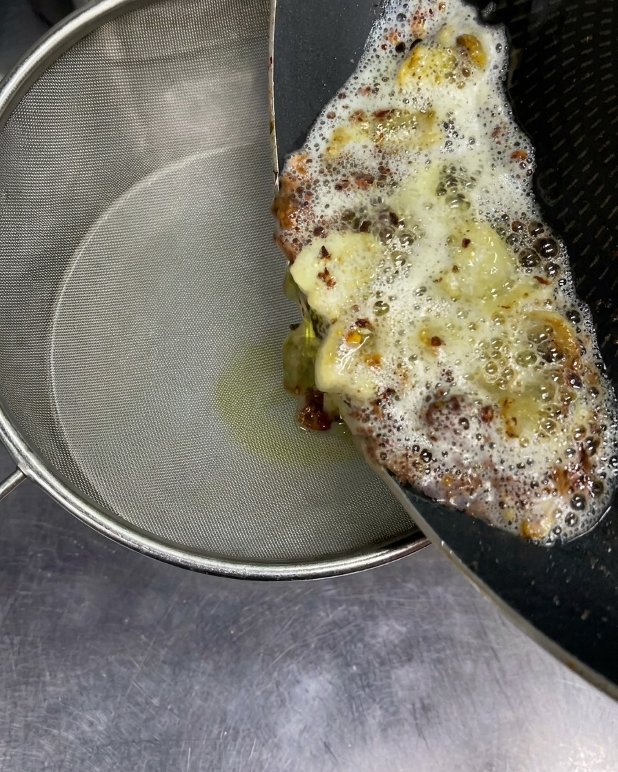 Huile brûlante avec des morceaux dail frit versée dans un tamis fin au-dessus dune pomme.