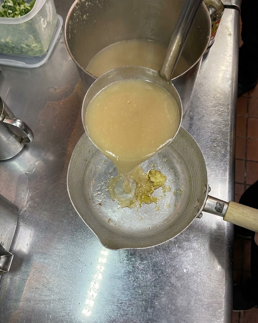 Louche versant du bouillon chaud dans une petite casserole contenant les assaisonnements.
