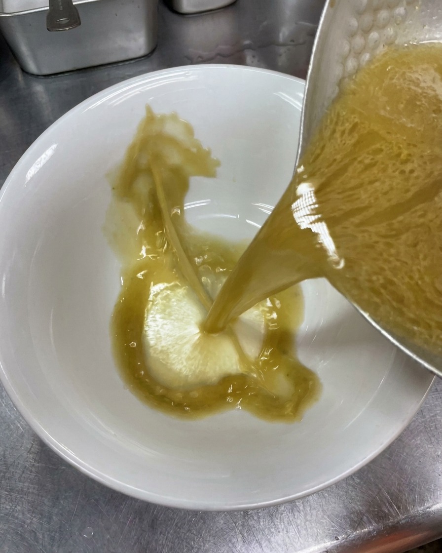 Bouillon tonkotsu opaque versé dune casserole dans un bol à ramen en céramique blanche.