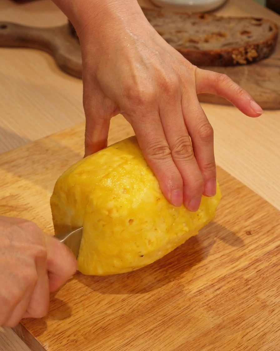 Mains découpant un ananas frais pelé sur une planche à découper en bois.