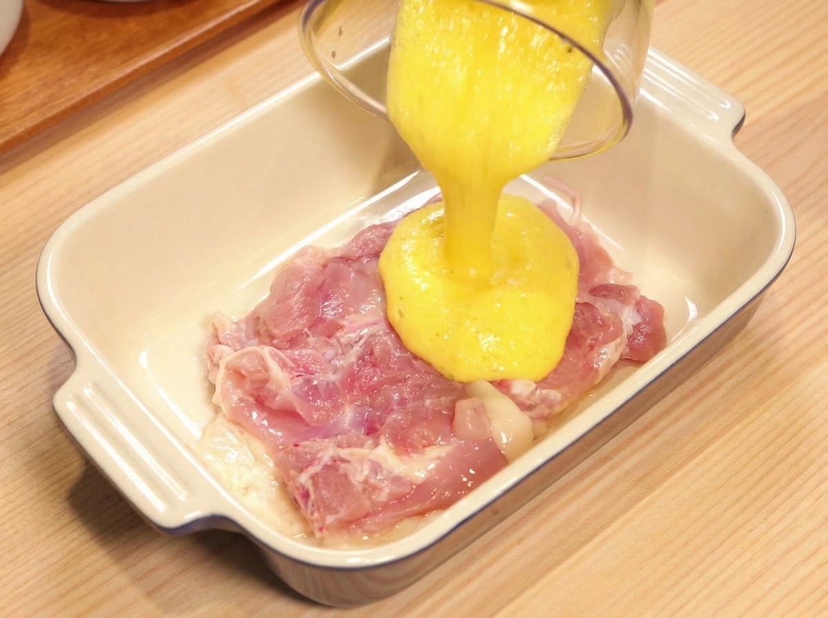 Verser du jus dananas frais sur une cuisse de poulet crue dans un plat en céramique blanc.
