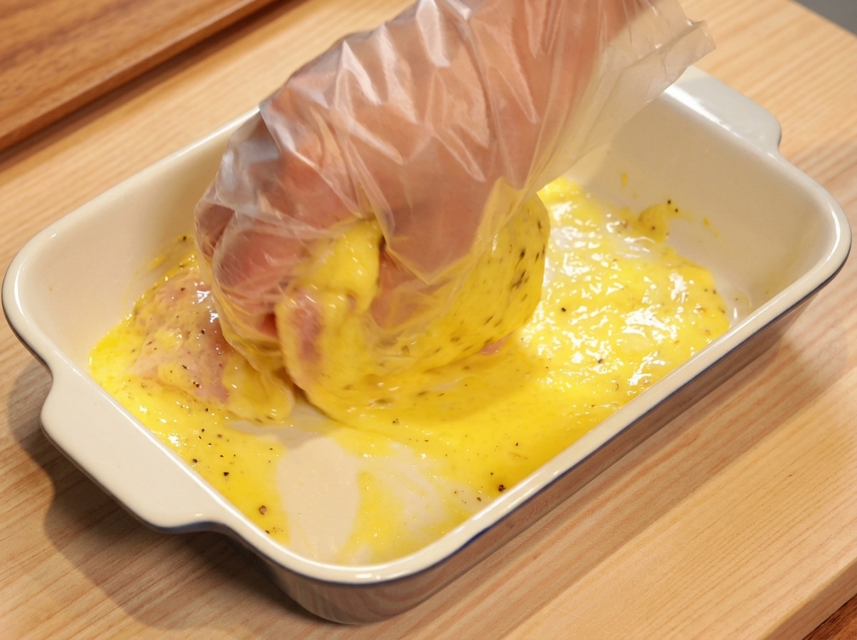 Une main gantée massant une cuisse de poulet crue dans une marinade à lananas jaune vif.
