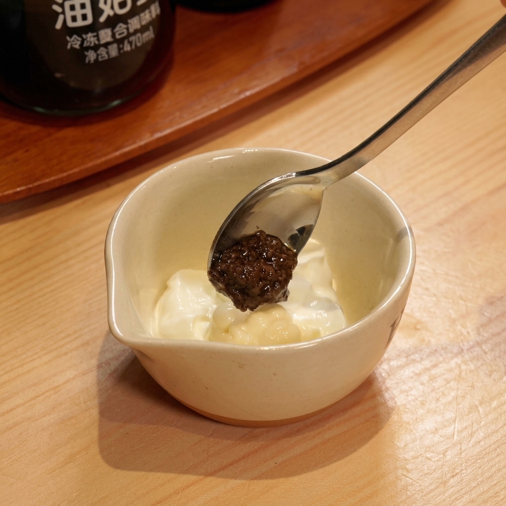 Une cuillère de pâte de truffe noire au-dessus dun bol de sauce au yaourt crémeuse.