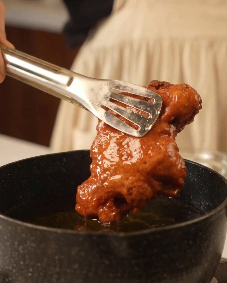 Pince métallique soulevant un morceau de poulet frit bien doré et croustillant.