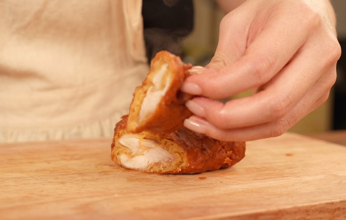 Doigts tenant un morceau de poulet coupé en deux montrant une croûte dorée et une chair blanche juteuse.