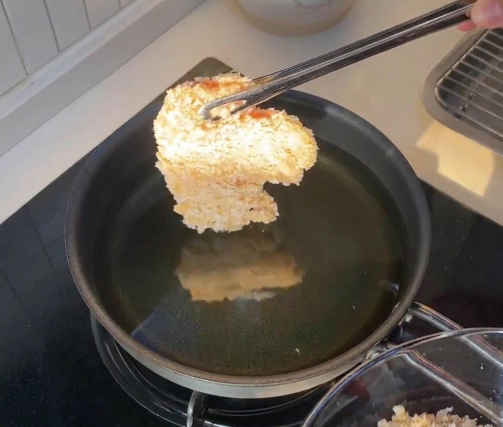 Filet de poulet pané tenu par une pince juste au-dessus dune poêle dhuile chaude.