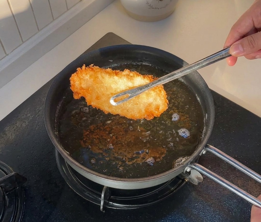 Pince soulevant un morceau de poulet frit doré hors de la poêle dhuile chaude.