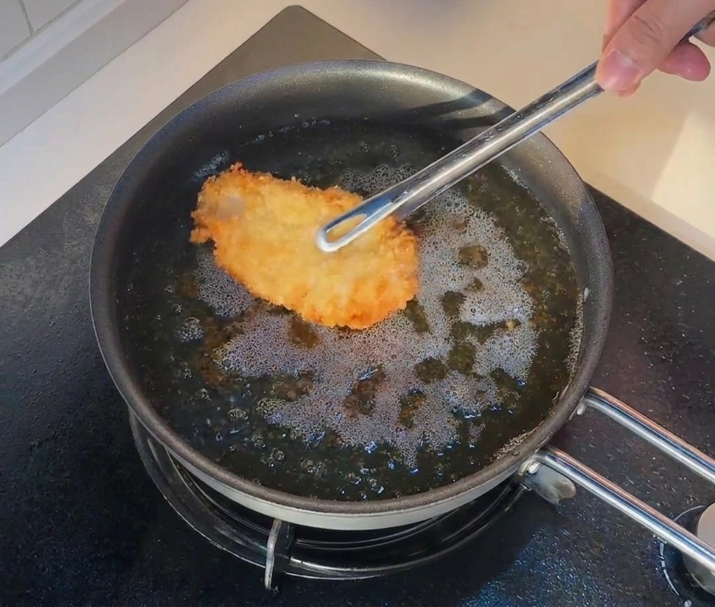 Pince replaçant un morceau de poulet frit dans lhuile très chaude pour un deuxième bain.