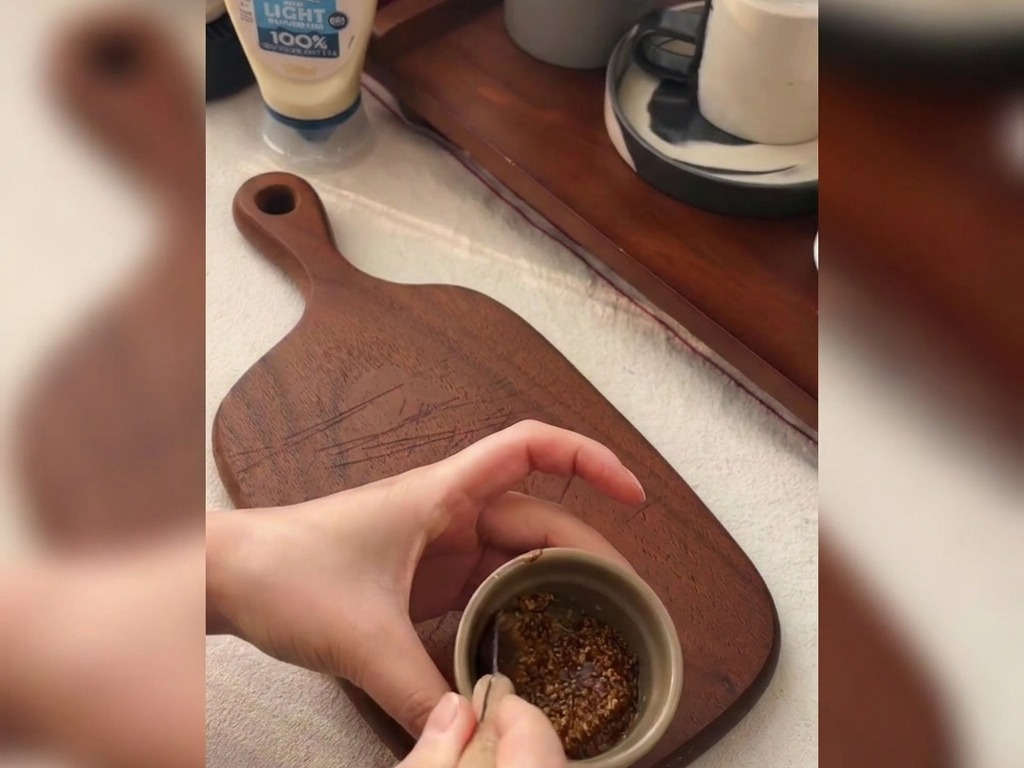 Mains mélangeant de la moutarde à lancienne et du miel dans un petit bol sur une planche à découper.