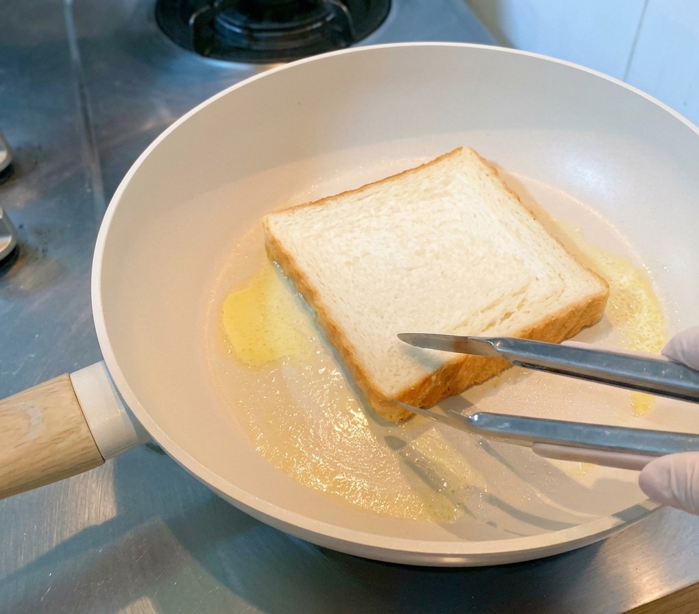 Une tranche de pain de mie blanc dorant dans le beurre fondu à lintérieur dune poêle.