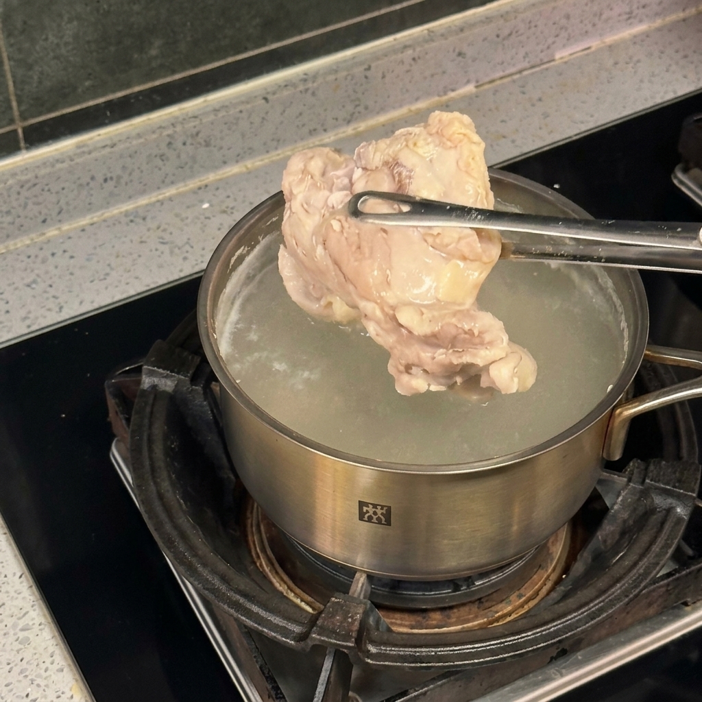 Un morceau de poulet tenu par une pince au-dessus dune casserole deau bouillante.
