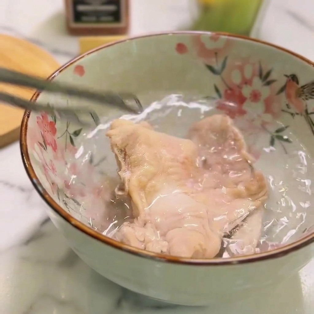 Un morceau de poulet cuit plongé dans un bol deau froide à laide dune pince.