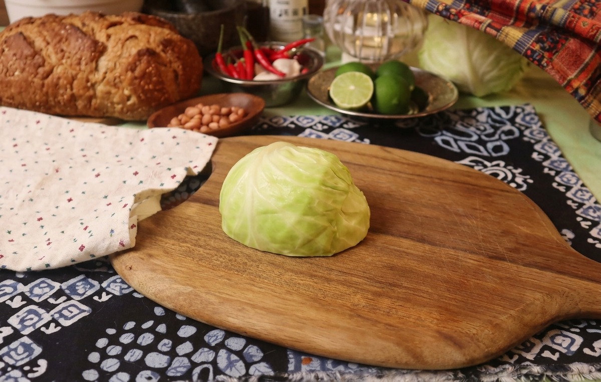 Un quart de chou vert frais sur une planche à découper en bois à côté dun linge à motifs rustiques.