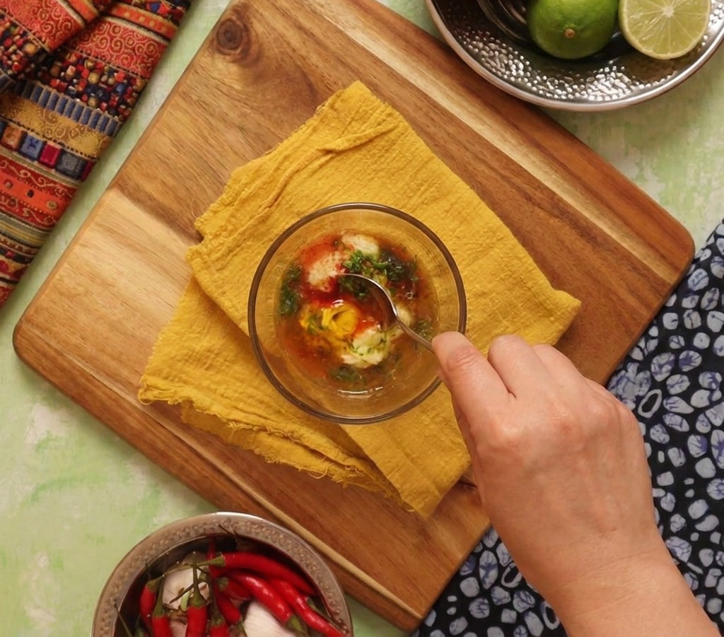 Une main remuant un bol de sauce crémeuse orange faite de mayonnaise, citron vert et épices avec une cuillère.