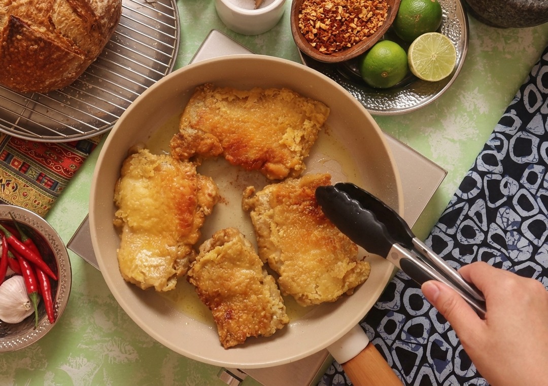Pinces de cuisine retournant un morceau de poulet dans la poêle, révélant une surface parfaitement dorée et croustillante.