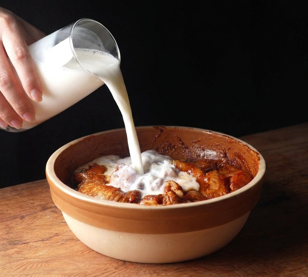 Versement de lait fermenté depuis un pichet en verre sur le poulet mariné dans un bol.