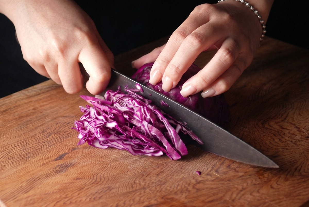 Une personne éminçant finement un chou rouge avec un couteau de chef sur une planche en bois.