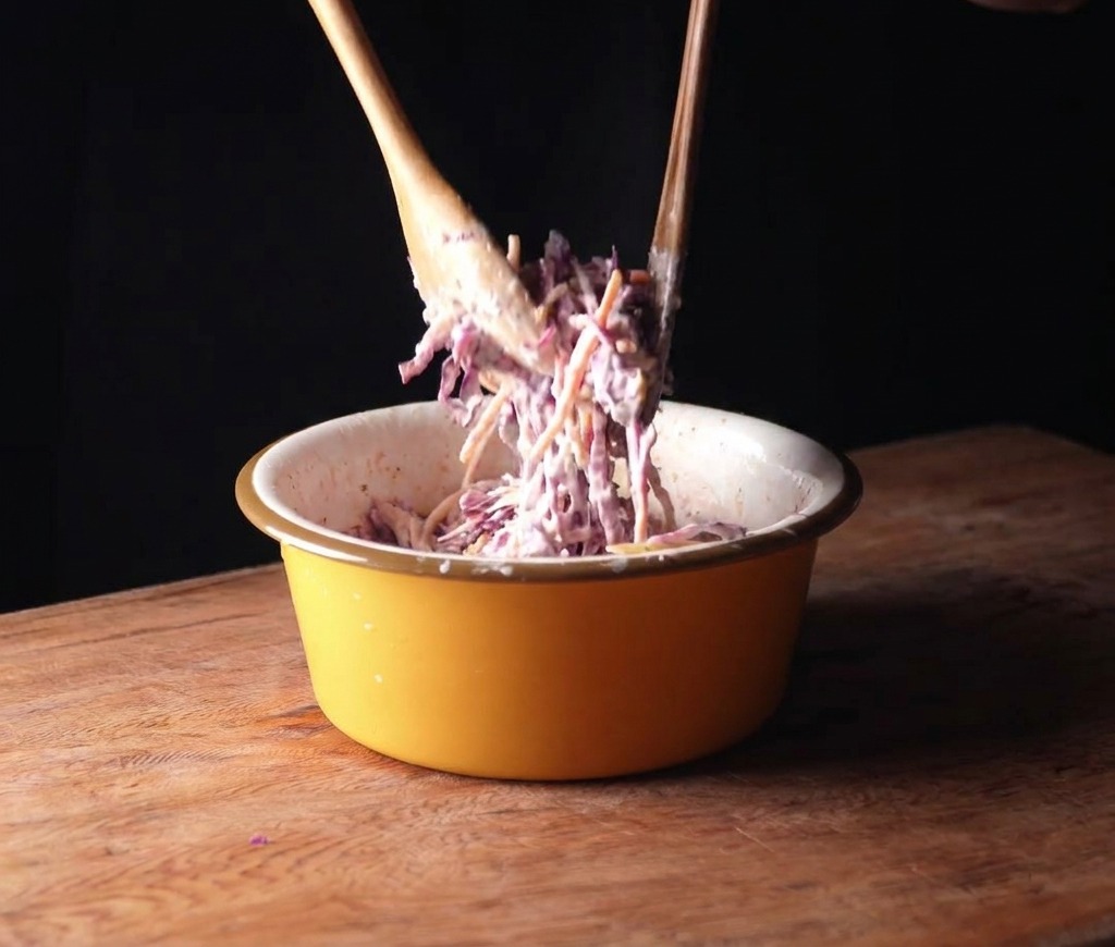 Mélange du chou rouge et des carottes avec une sauce crémeuse dans un bol jaune avec des cuillères en bois.
