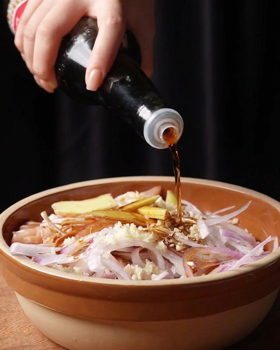 Main versant de la sauce soja et de la sauce de poisson sur les morceaux de poulet et les aromates.
