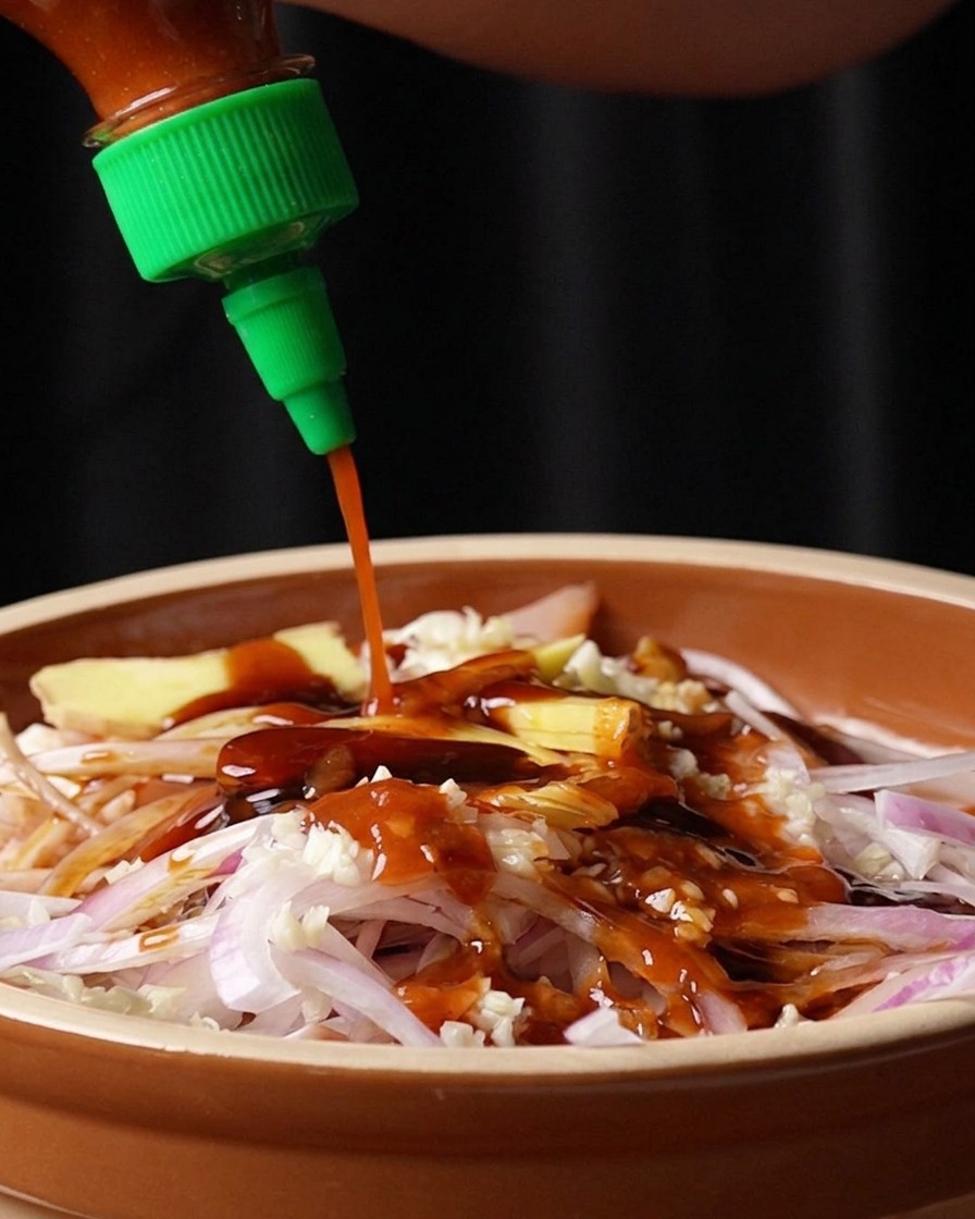 Sauce Sriracha rouge versée depuis une bouteille sur le mélange de poulet.