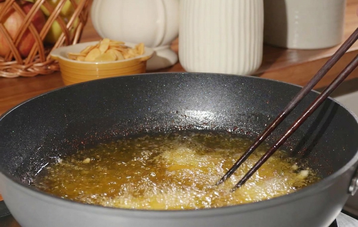 Morceau de poulet fariné déposé avec des baguettes dans lhuile de friture bouillonnante.