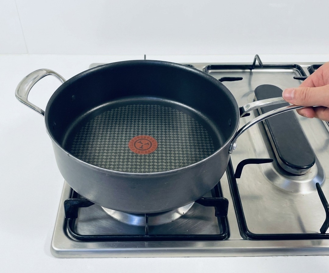 Une grande poêle antiadhésive posée sur une cuisinière à gaz avec le brûleur allumé.