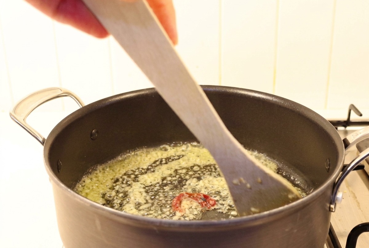 De lail haché et du piment mélangés au beurre fondu dans une poêle avec une spatule en bois.