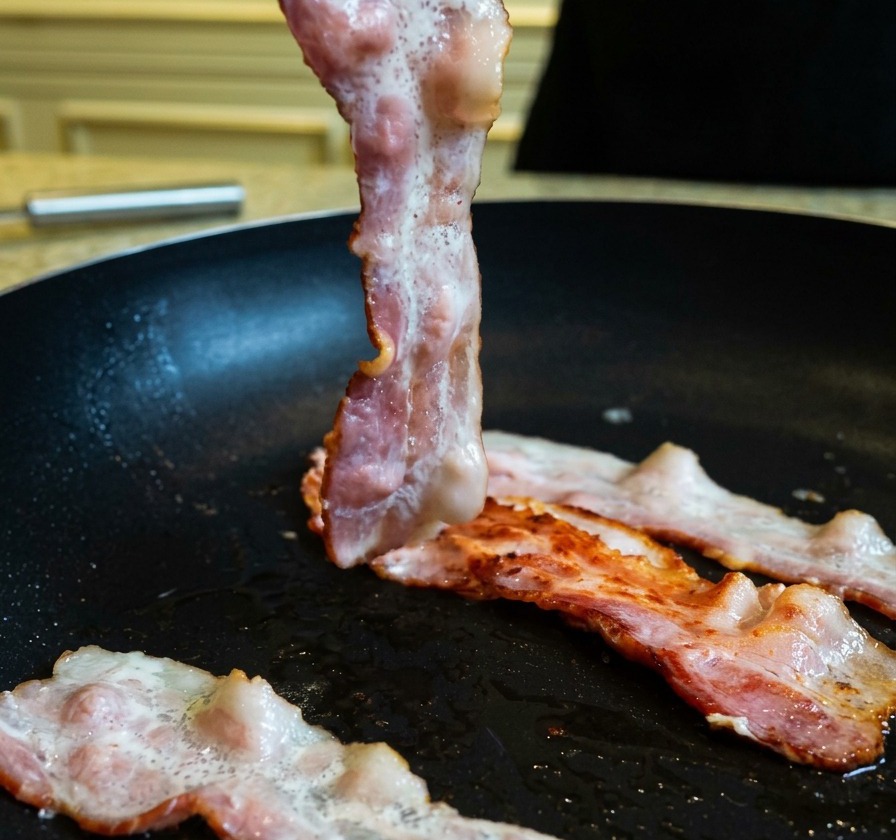 Soulèvement dune tranche de bacon partiellement cuite et dorée dans une poêle à laide dune pince de cuisine.